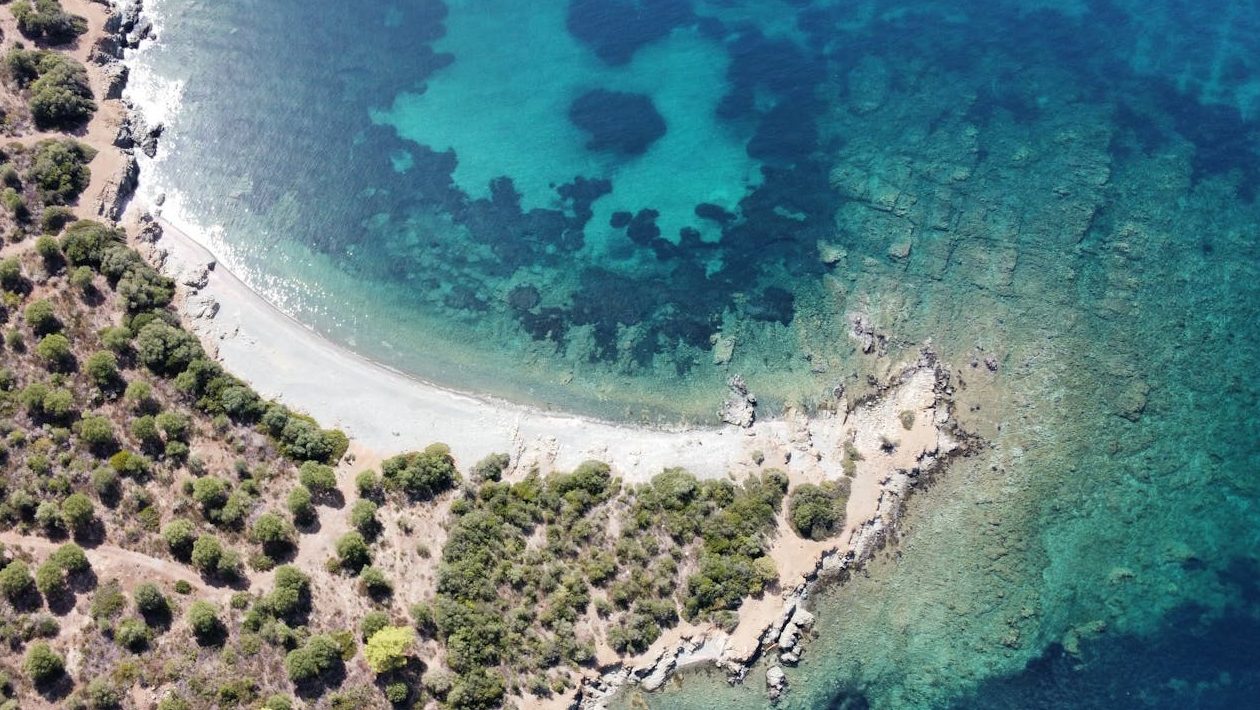 A stunning aerial shot of a Greek coastline with clear blue waters and lush greenery.