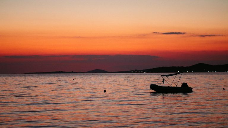 Silhouette of a boat at sunset on calm waters in Toroni, Greece. Perfect twilight tranquility.