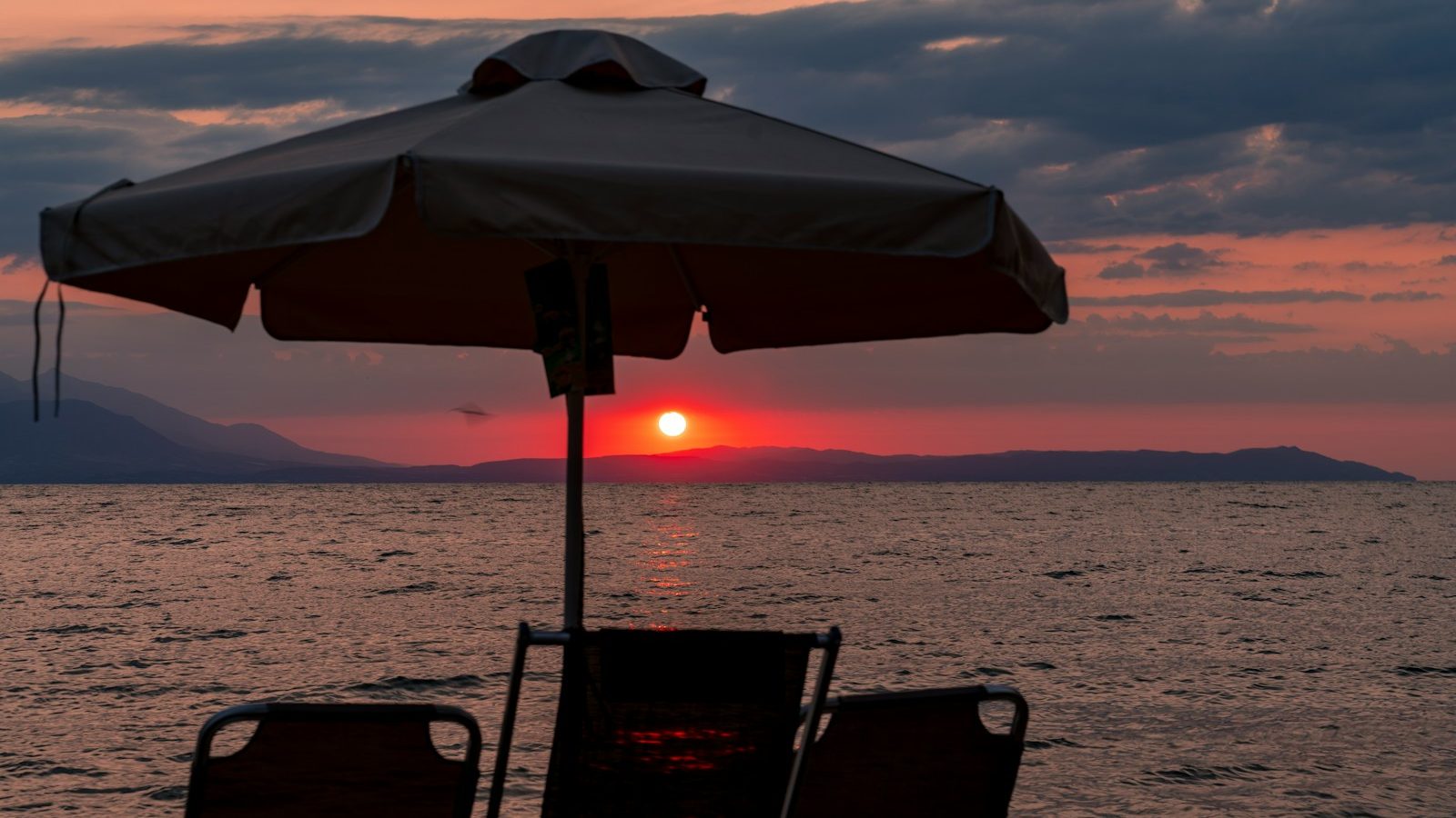 silhouette of two people sitting on chair under blue umbrella during sunset